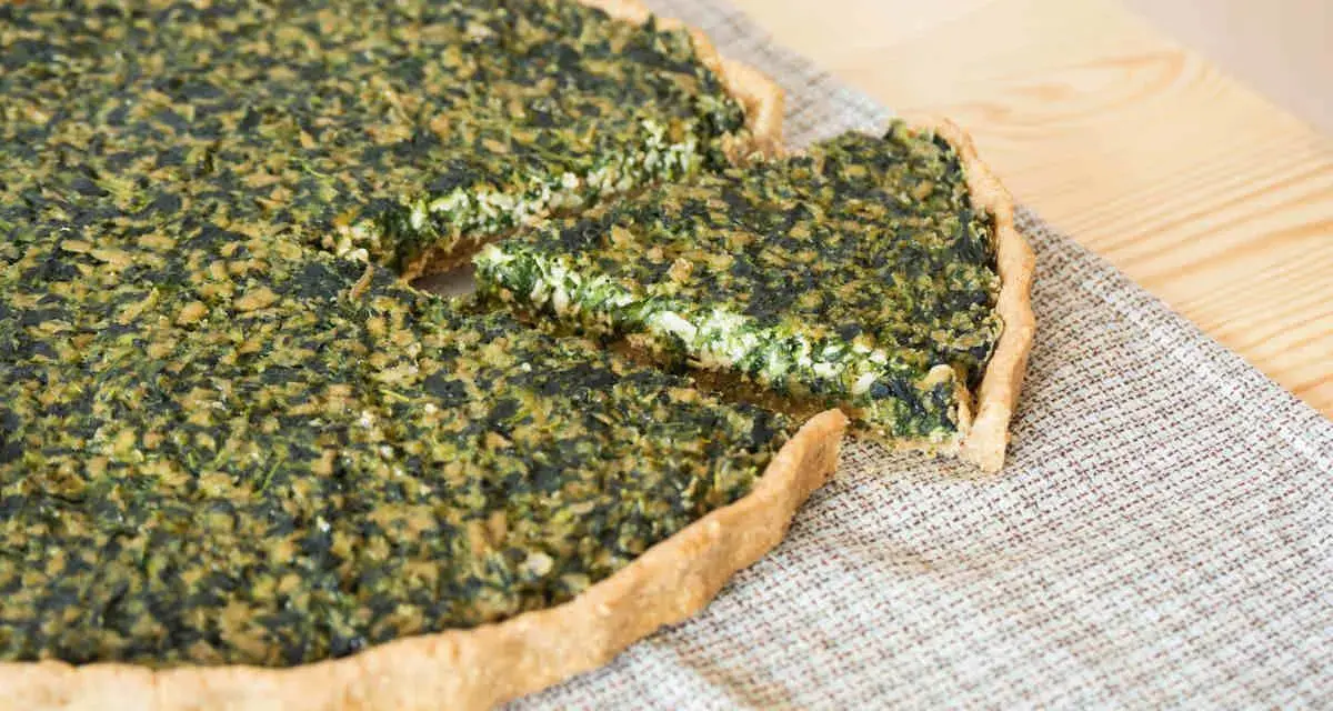 Una fetta di torta salata vegana spinaci, con una crosta dorata e un ripieno verde e cremoso, pronta per essere gustata.
