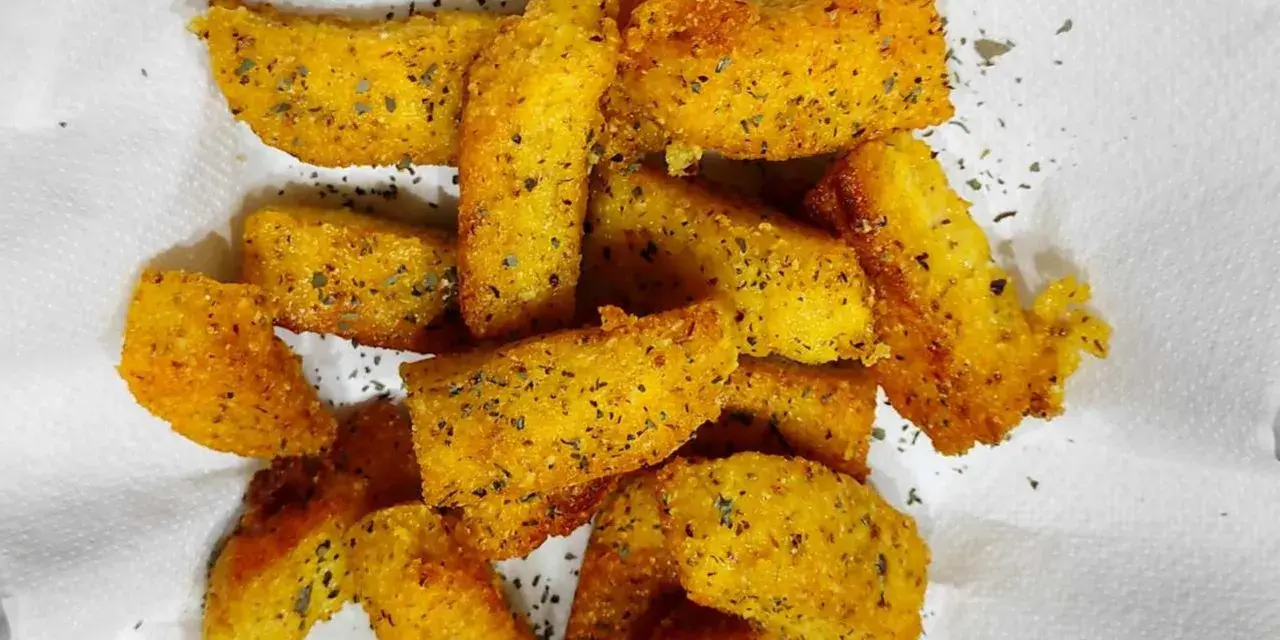 Croccanti bastoncini di polenta taragna fritta, dorati e conditi con erbe aromatiche, adagiati su carta bianca.
