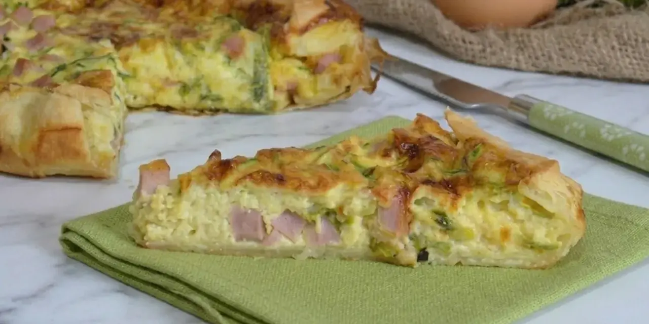 A slice of ham and zucchini quiche on a green napkin, with the rest of the quiche in the background.