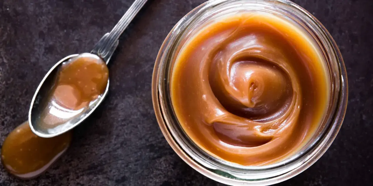 Un cucchiaio pieno di crema pasticcera al caramello salato, accanto a un barattolo dello stesso delizioso composto.