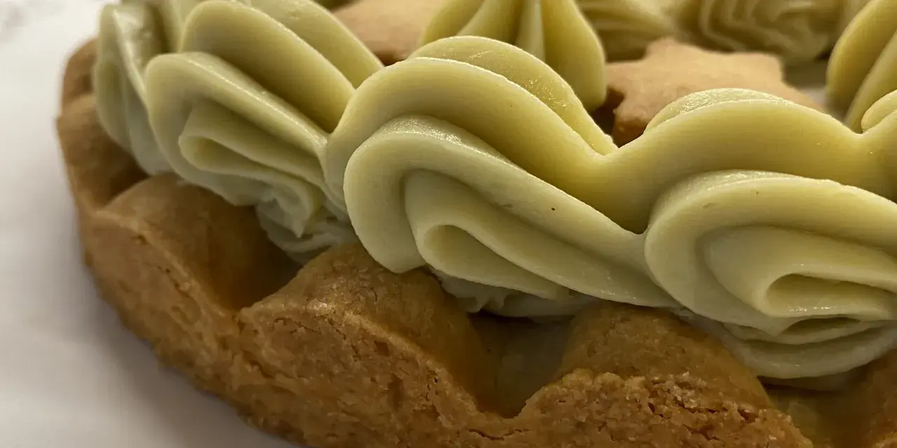 Torta con bordi croccanti e un abbondante strato di ganache pistacchio, decorata con biscotti a forma di stella.