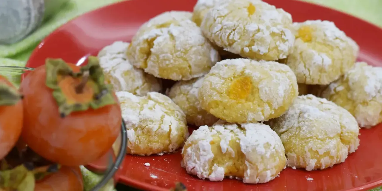 Biscotti ai cachi, dolcetti morbidi e profumati, cosparsi di zucchero a velo, accanto a cachi freschi.
