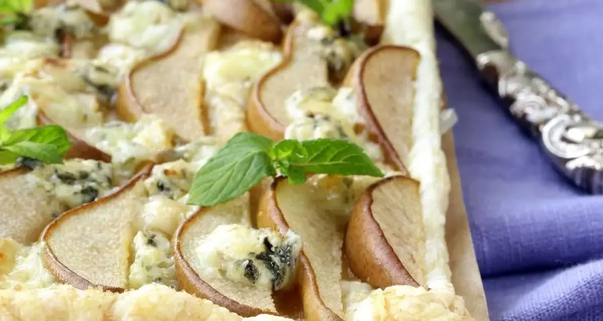 Deliziosa pizza zola e pere su pasta sfoglia croccante, guarnita con foglie di menta fresca. Un connubio di sapori unico.