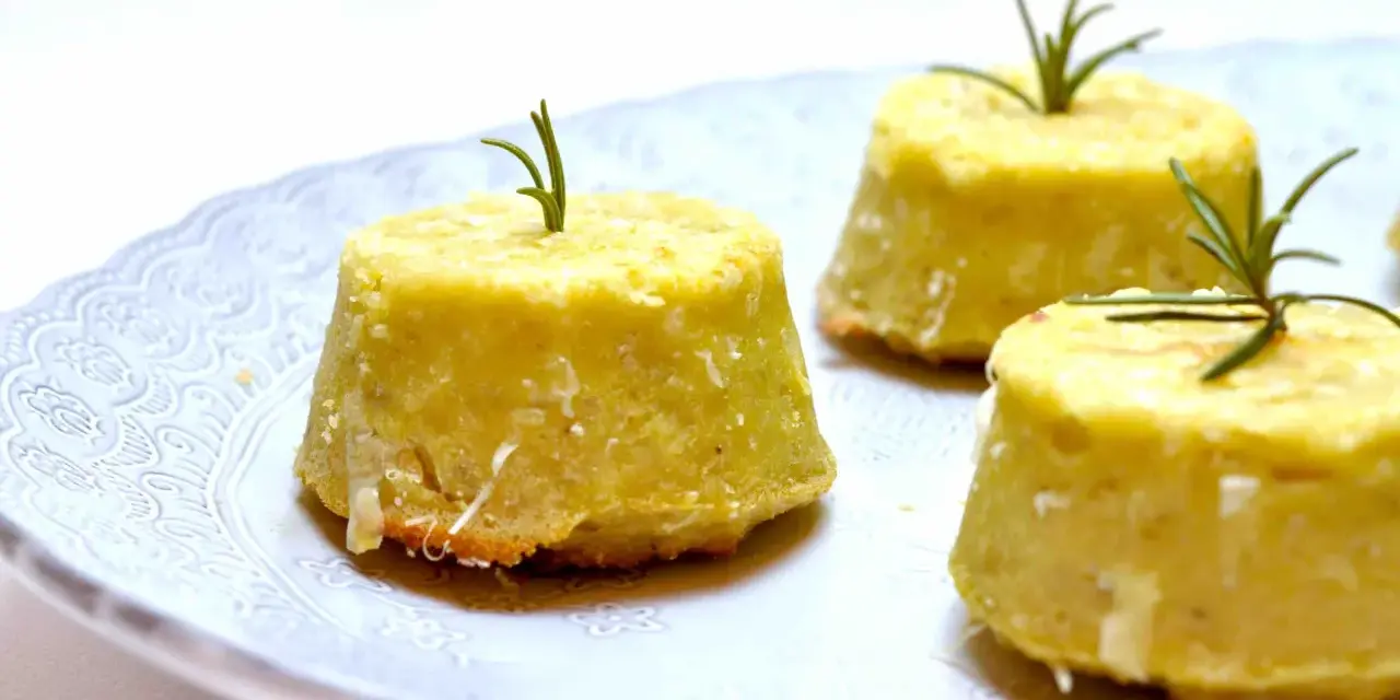 Flan di topinambur senza patate, dorati e profumati, guarniti con rosmarino fresco su un piatto bianco decorato.
