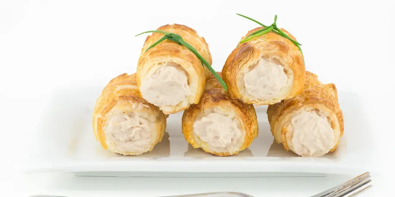 Cannoli salati ripieni di tonno, guarniti con erba cipollina, su un piatto bianco con forchetta.