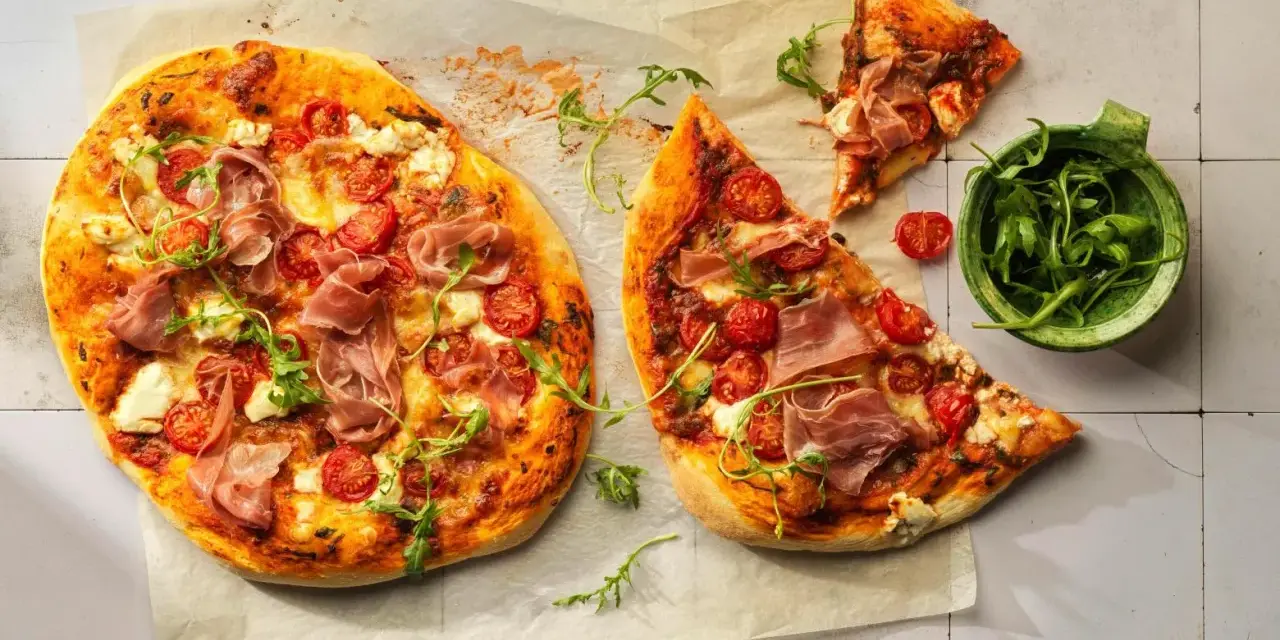 Pizza con mascarpone, pomodorini, prosciutto crudo e rucola, su carta forno.