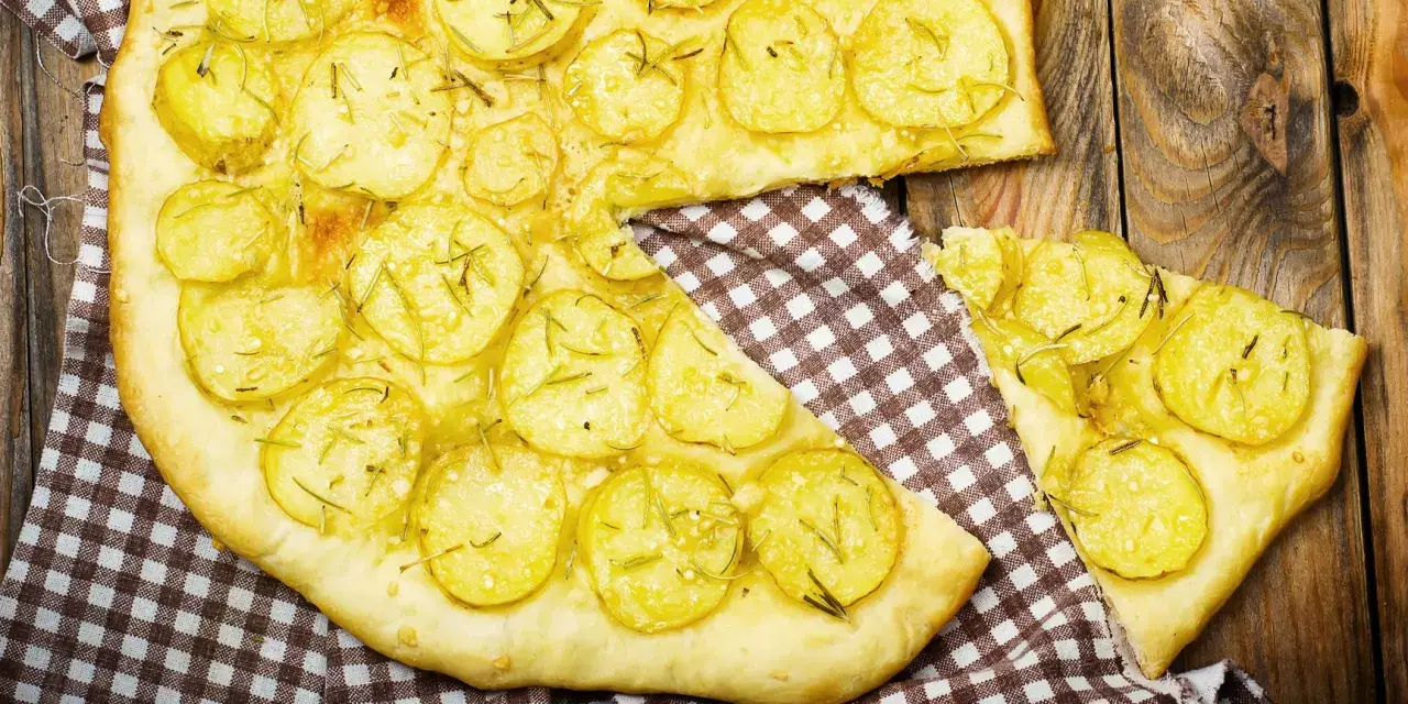Schiacciata di patate con farina di ceci, guarnita con rosmarino fresco, su un tagliere di legno rustico.