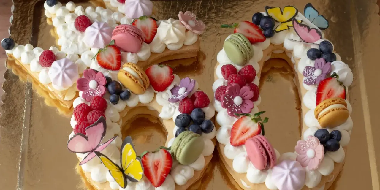 Una torta numero 60 decorata con panna, frutta fresca, macarons e farfalle. Una deliziosa ricetta torta numero per festeggiare.