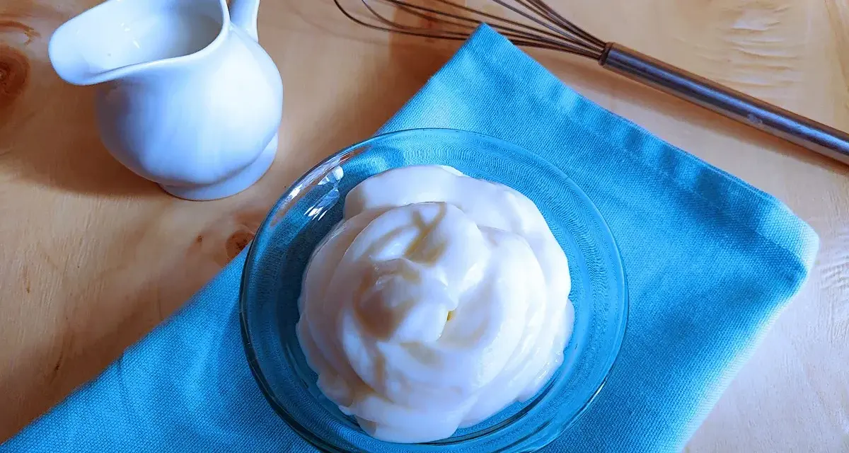 Crema soffice e vellutata, una delizia preparata con yogurt greco. Accanto, una piccola brocca e una frusta, pronti per creare altre bontà.