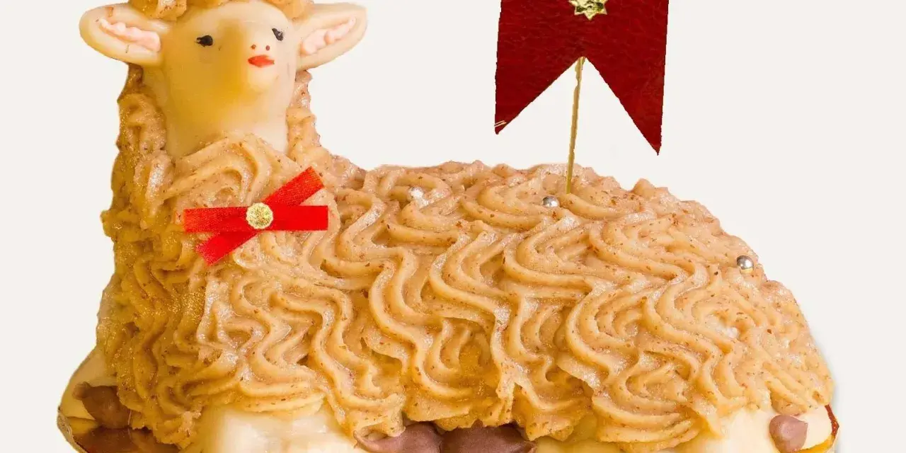 A decorative cake shaped like a lamb, with piped frosting and a red ribbon.