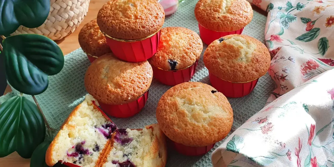 Morbidi muffin ai mirtilli, uno tagliato a metà rivela il suo interno succoso. Perfetti per una colazione o merenda golosa.