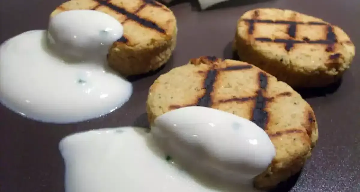 Deliziosi medaglioni di ceci grigliati, serviti con una salsa bianca cremosa e guarniti con erbe aromatiche.
