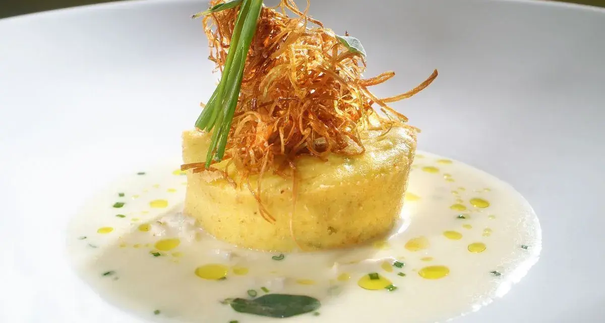 Flan di porri con salsa di acciughe, guarnito con cipolla croccante e erbe aromatiche. Un piatto raffinato che celebra i sapori del mare e della terra.