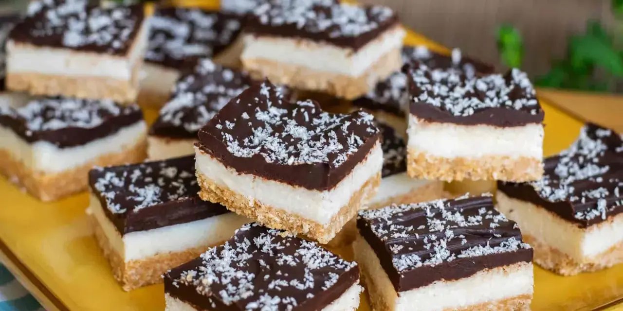 Deliziosi quadrotti cioccolato e cocco, stratificati con base croccante, crema bianca e copertura fondente, spolverati con cocco grattugiato.