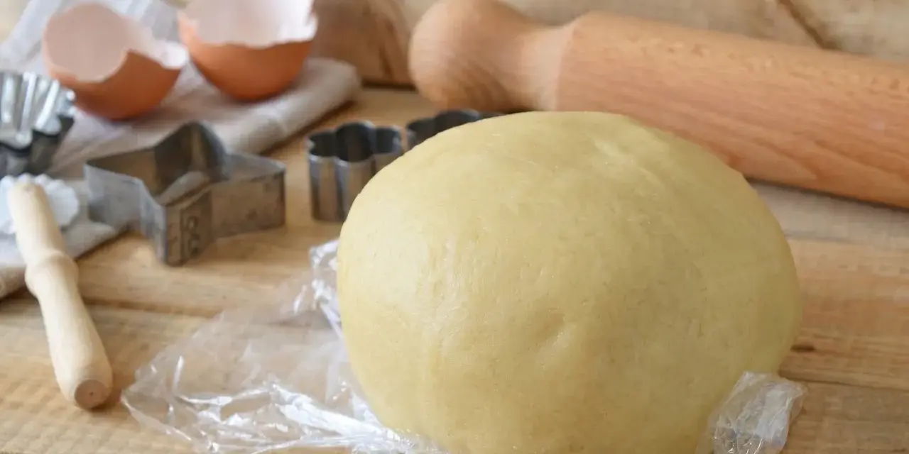 Impasto per kruche ciasto, stampini per biscotti, gusci d'uovo e mattarello pronti per preparare dolci deliziosi.