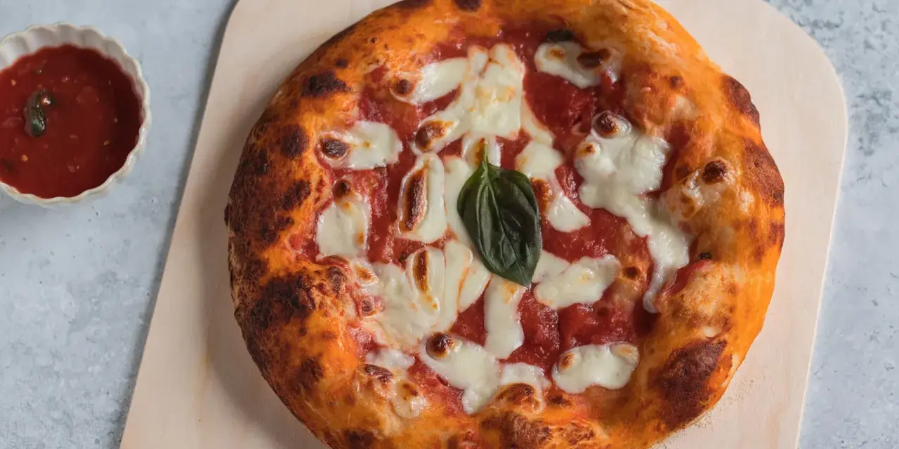 Pizza napoletana appena sfornata, con pomodoro, mozzarella filante e basilico fresco, pronta per essere gustata.