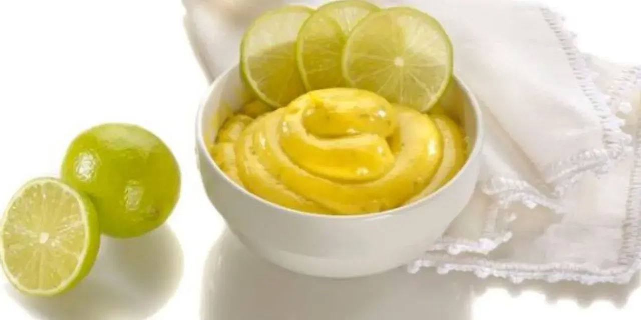 Una ciotola di cremosa crema al lime, guarnita con fette di lime fresco e accompagnata da lime interi e a metà.