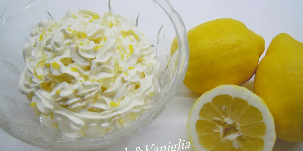 Una ciotola di panna montata con scorza di limone, accanto a limoni freschi. Perfetta per una ganache al limone leggera e profumata.