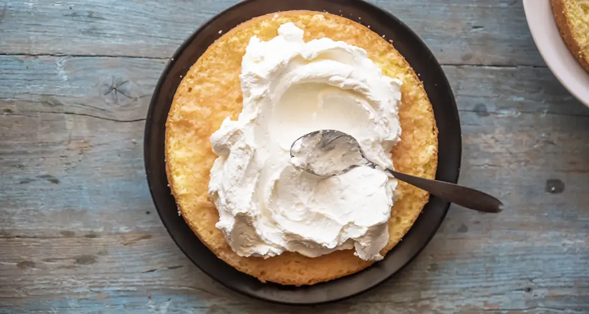Una fetta di pan di spagna attende la sua deliziosa crema allo yogurt, spalmata con un cucchiaino.
