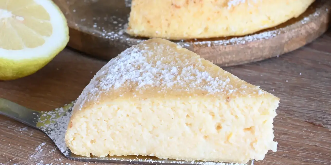 Una fetta di torta con semola, spolverata di zucchero a velo, accanto a un limone fresco.