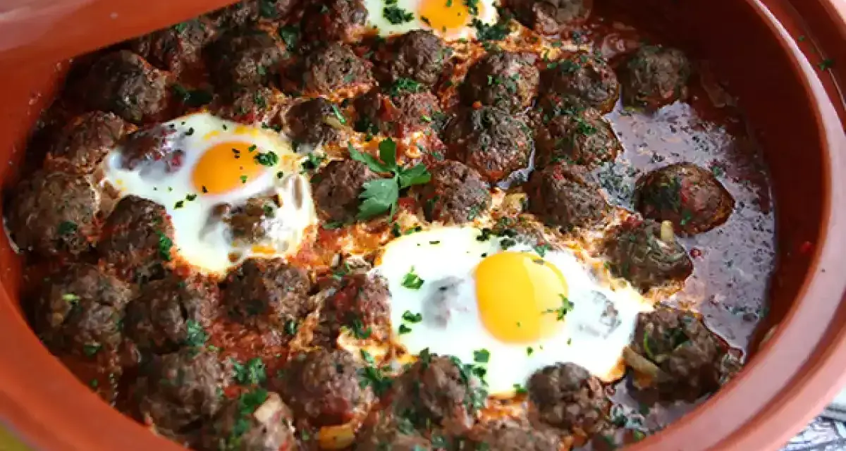 Polpette marocchine in umido con uova cotte nel tajine, guarnite con prezzemolo fresco.