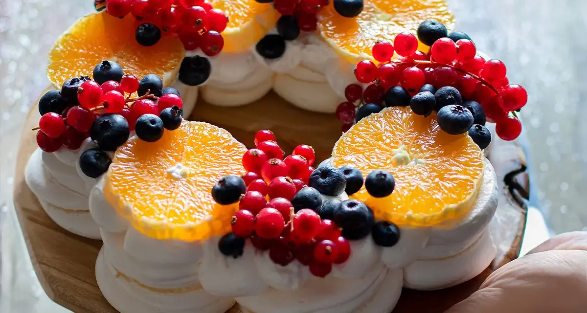 Delizioso tort pavlova a forma di corona, decorato con fette d'arancia, ribes rosso e mirtilli.