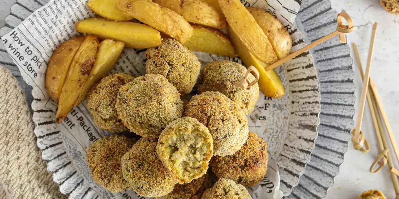 Polpette di verza e ricotta dorate e croccanti, servite con spicchi di patate fritte su carta di giornale.