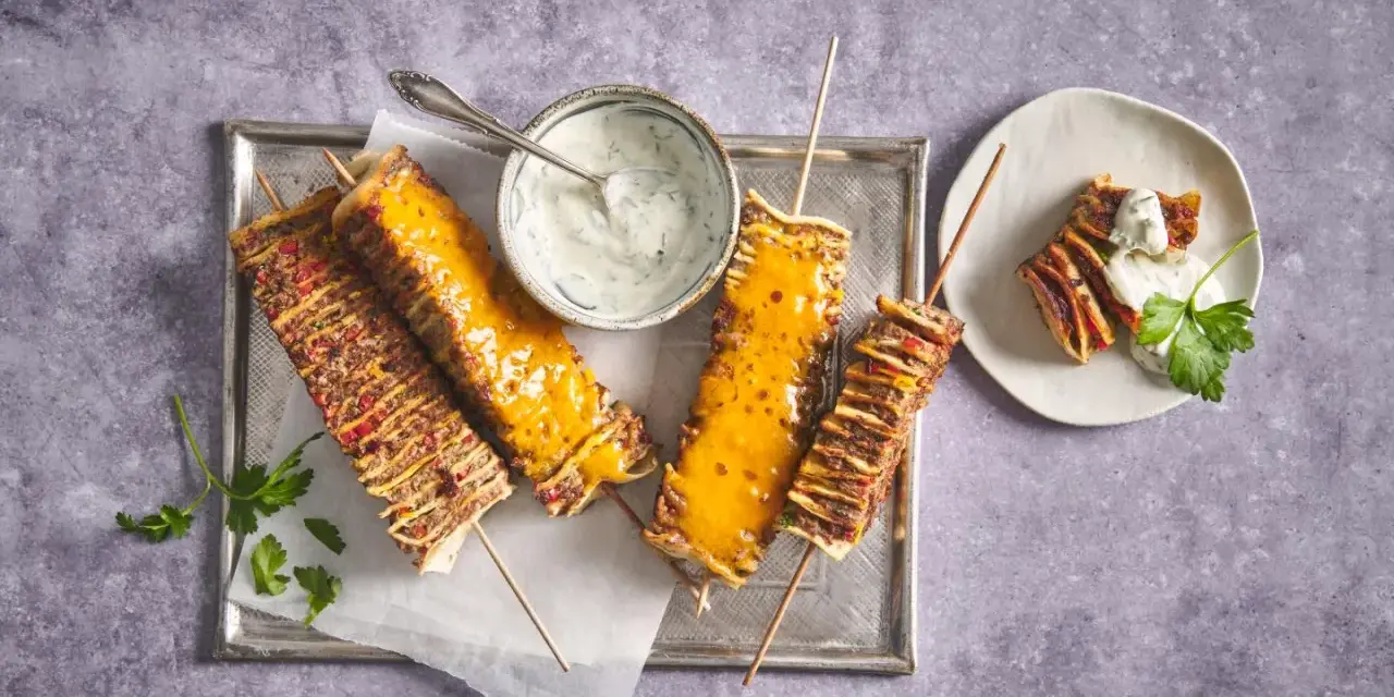 Tortilla kebab su spiedini, alcuni ricoperti di formaggio fuso, serviti con salsa allo yogurt e prezzemolo.