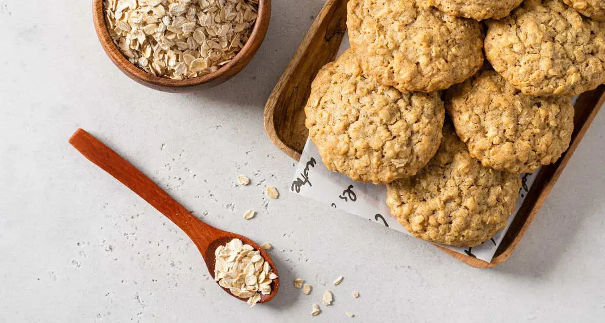 Biscotti di avena dorati e croccanti, con fiocchi d'avena in una ciotola e un cucchiaio.