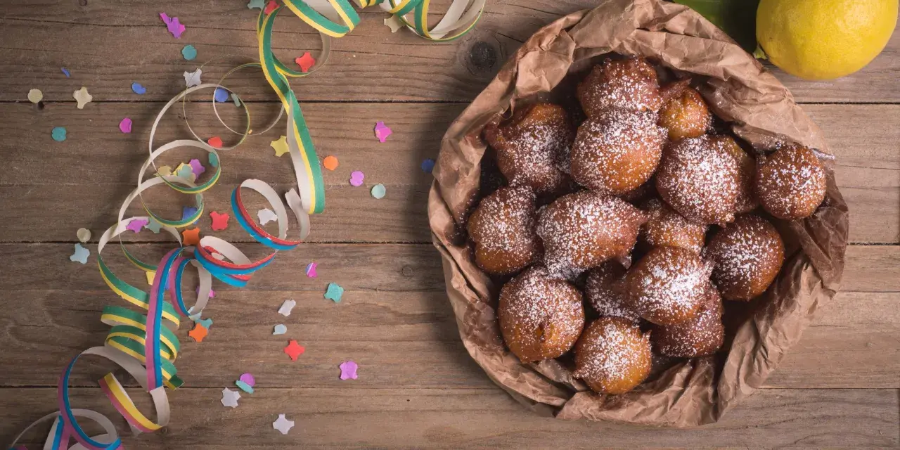 Castagnole abruzzesi cosparse di zucchero a velo, pronte per Carnevale, con coriandoli e stelle filanti su tavola di legno.