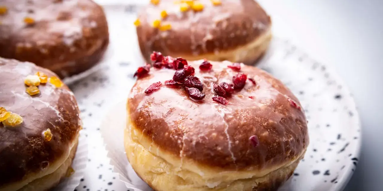 Paczki ricchi e golosi, con glassa lucida e decorazioni di frutta secca. Un invito a provare il paczki przepis perfetto.