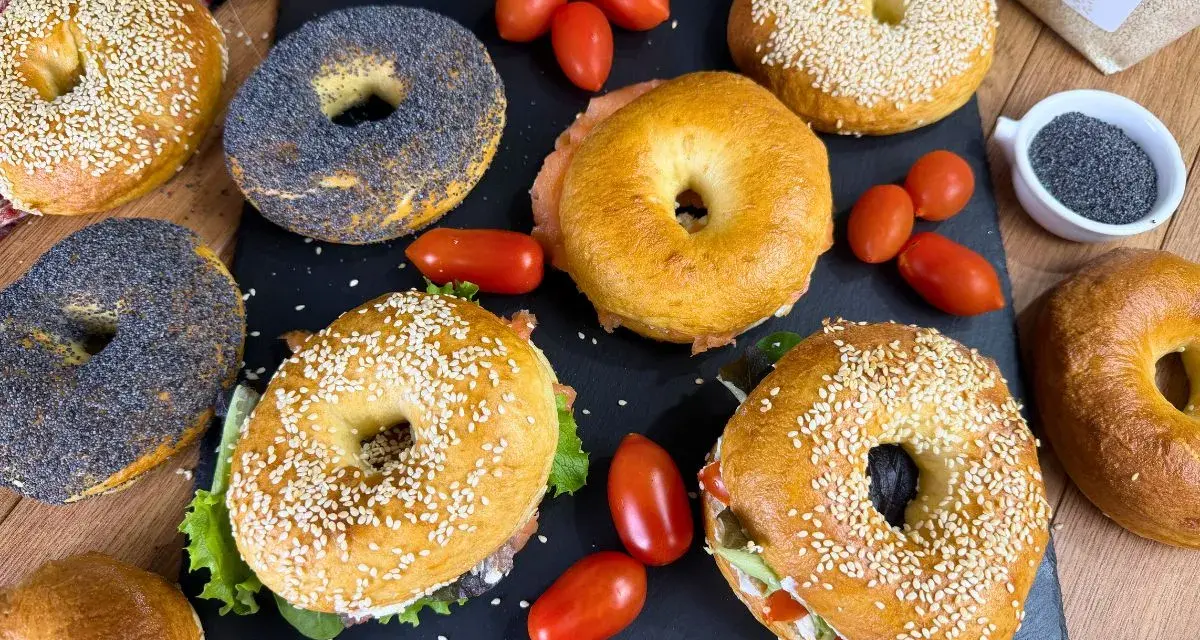 Varietà di bagel dolci e salati, alcuni con semi di sesamo, altri con semi di papavero, accompagnati da pomodorini e salmone affumicato.