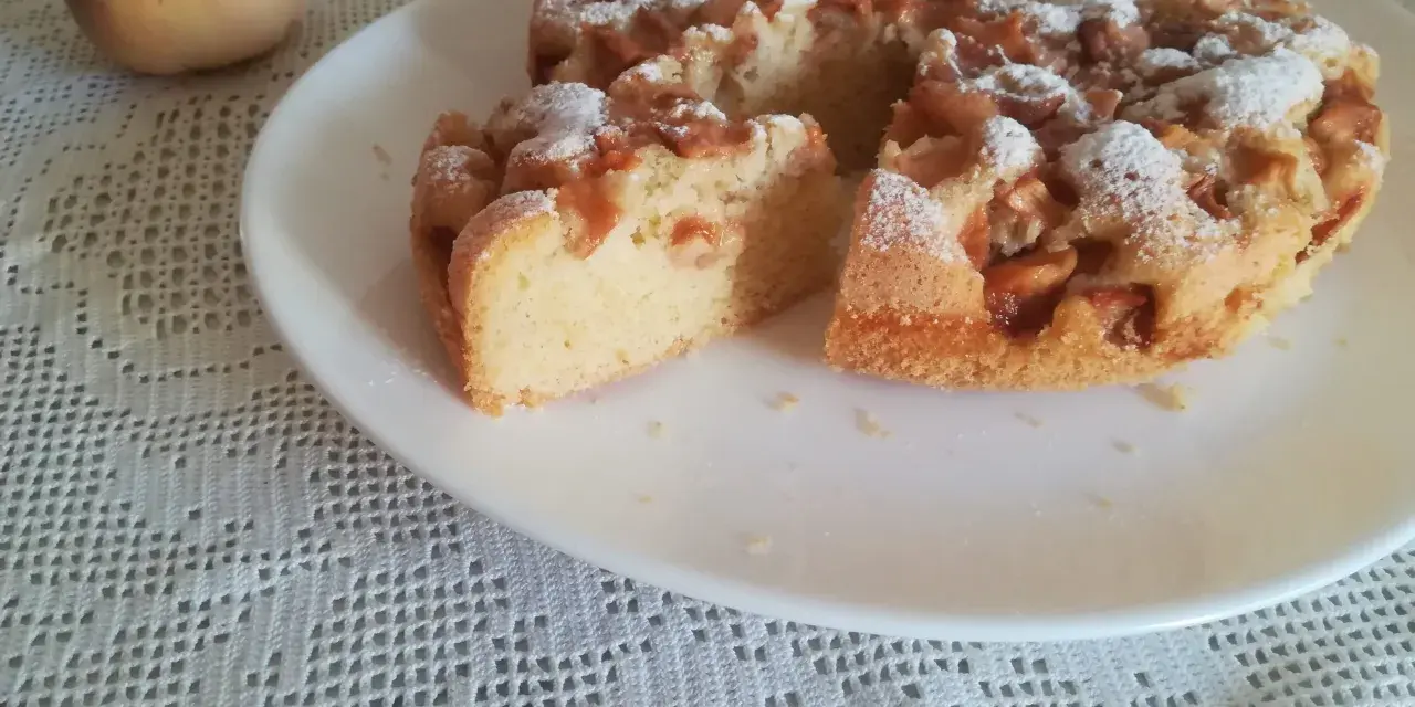 Delizioso ciasto z brzoskwiniami, cosparso di zucchero a velo, su un piatto bianco, accanto a una pesca fresca.