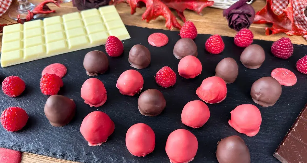 Cioccolatini al lampone, alcuni ricoperti di cioccolato fondente, altri di rosa, con lamponi freschi e tavoletta di cioccolato bianco.