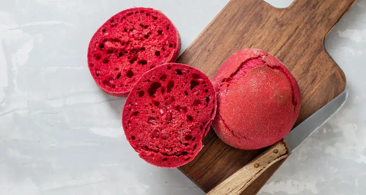 Pane alla barbabietola, un panino rosso vibrante tagliato a metà su un tagliere di legno, pronto per essere gustato.