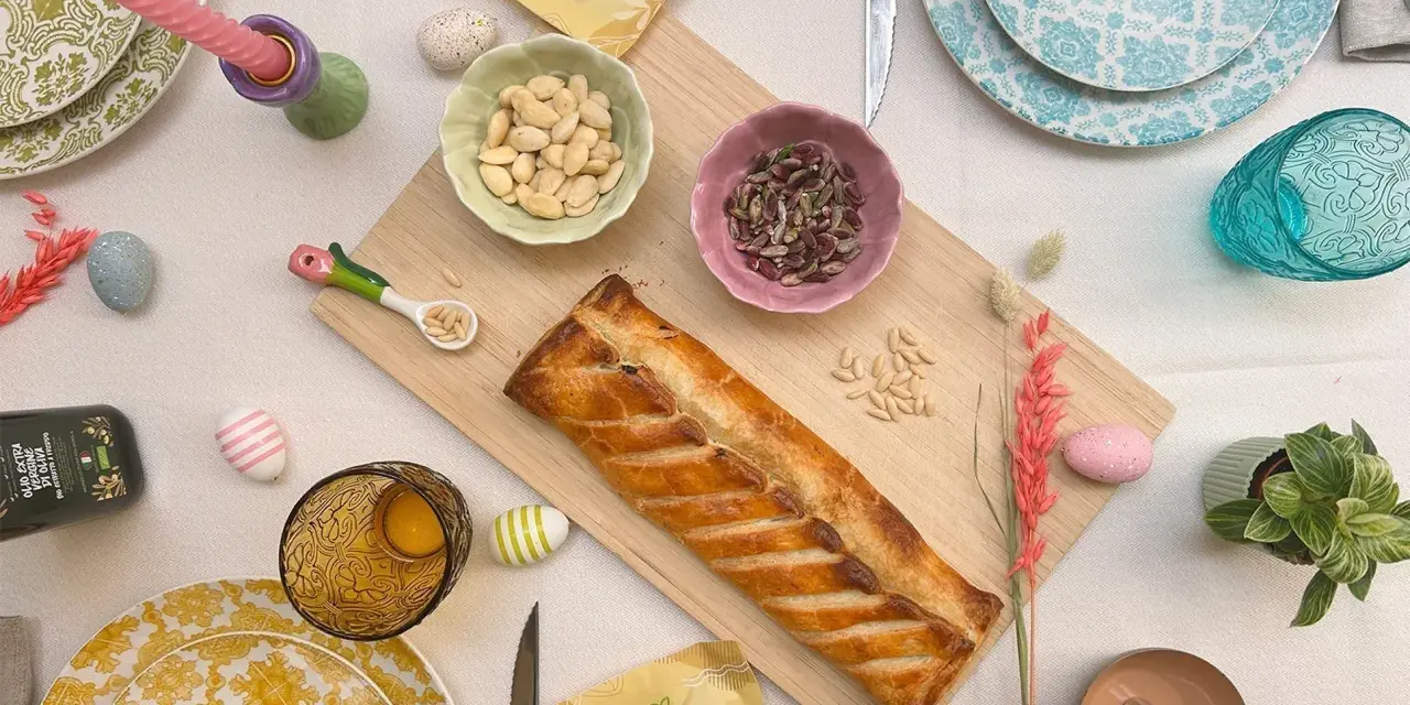 Torta pasqualina senza uova dorata, con mandorle e pinoli, decorata con uova colorate e candela pasquale.