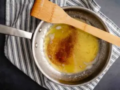 Burro alla nocciola che si scioglie in padella, con una spatola di legno appoggiata sopra.