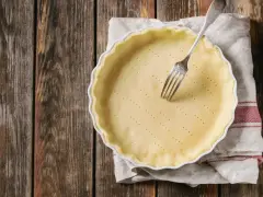 Pasta frolla salata con olio e parmigiano pronta per essere infornata. Una forchetta è appoggiata sulla base bucherellata.