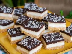 Deliziosi quadrotti cioccolato e cocco, stratificati con base croccante, crema bianca e copertura fondente, spolverati con cocco grattugiato.