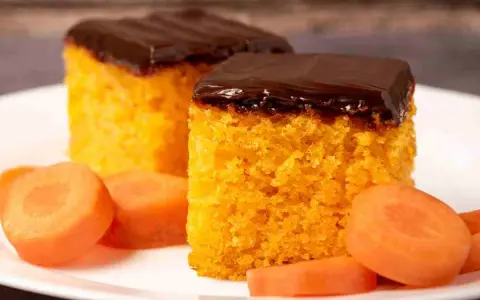 Due fette di ciasto marchewkowe, soffice e arancione, ricoperte di glassa al cioccolato fondente, con fettine di carota fresca intorno.