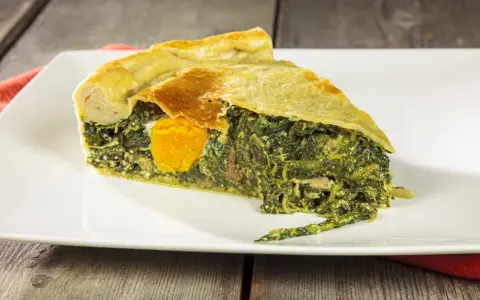 Una fetta di torta di bietole e ricotta senza sfoglia, con un uovo intero al centro, su un piatto bianco.