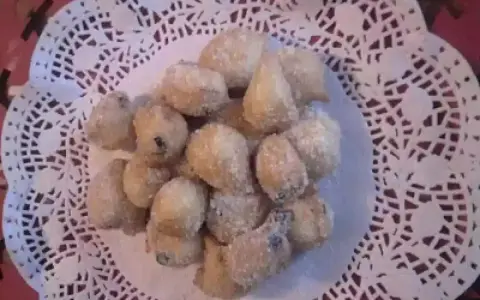 Un mucchietto di castagnole montersino, dolcetti dorati e zuccherati, adagiati su un centrino di pizzo bianco.