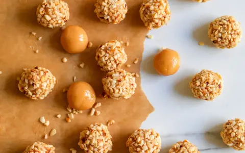 Piccoli bomboloni caramelle ricoperti di noccioline tritate, alcuni con un ripieno di caramello visibile.