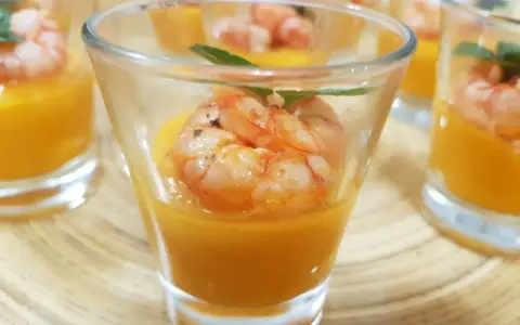 Deliziosi gamberi aperitivo in bicchierini con crema arancione e foglioline verdi.