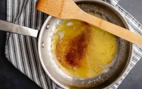 Burro alla nocciola che si scioglie in padella, con una spatola di legno appoggiata sopra.