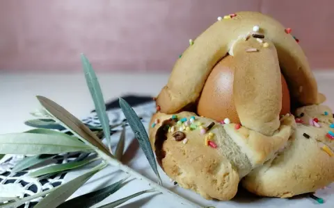 Dolci biscotti con uovo sodo, decorati con zuccherini colorati, pronti per essere gustati. Un ramoscello d'ulivo completa la scena.