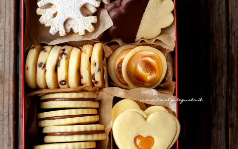 Scatola piena di deliziosi ciasteczka maślane: a fiocco di neve, al cioccolato, con ripieno di caramello e a forma di cuore.