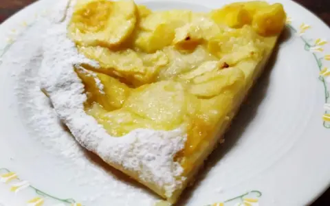Una fetta di pizza con le mele, cosparsa di zucchero a velo, su un piatto bianco con decorazioni floreali.