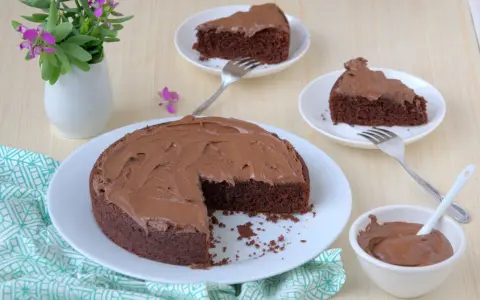 Deliziosa torta al cioccolato senza glutine con fecola di patate, ricoperta di glassa al cioccolato, servita su piatti bianchi con forchette.