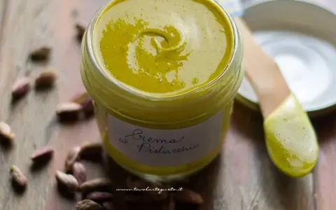 Un vasetto di cremosa crema di pistacchio, con pistacchi sparsi intorno. Perfetta per dolci e colazioni.